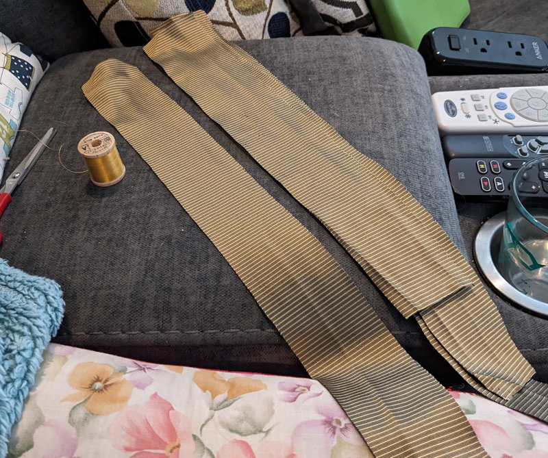 Strips of gold silk sitting on a couch console next to a spool of god silk thread.