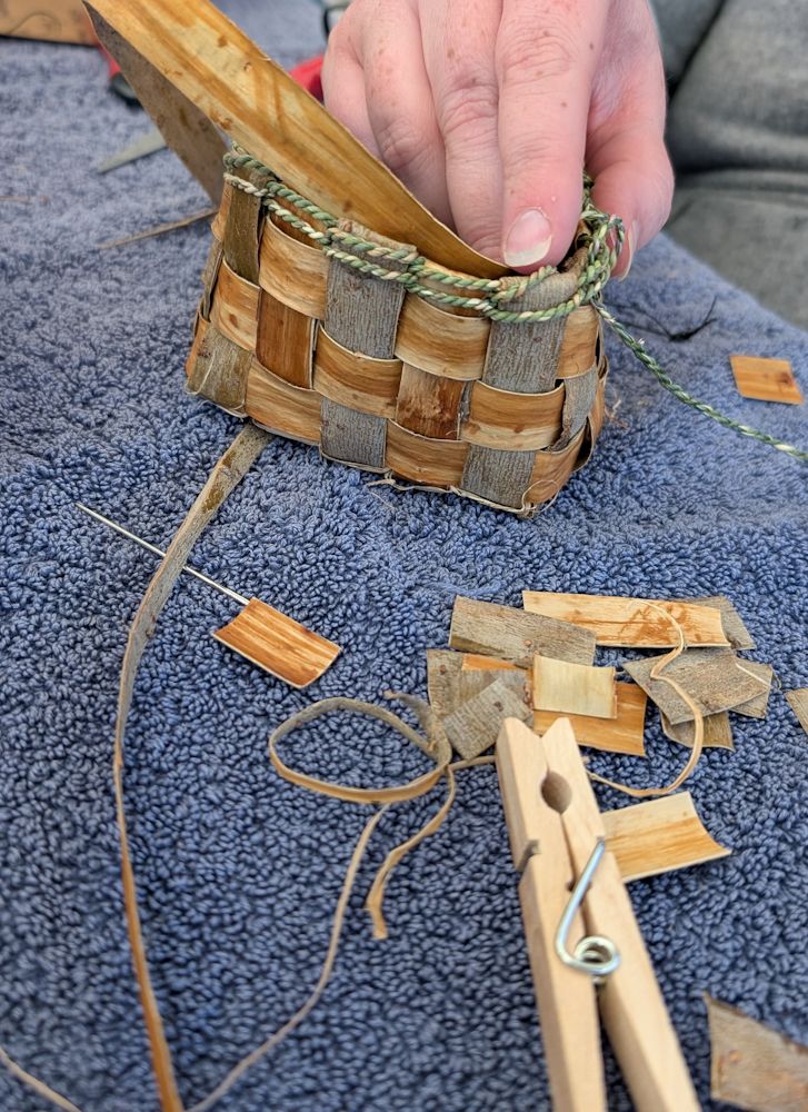 One student's basket: the willow strips vary between facing the interior and exterior, and a band at the top is being bound into place around the interior with sweetgrass cordage.