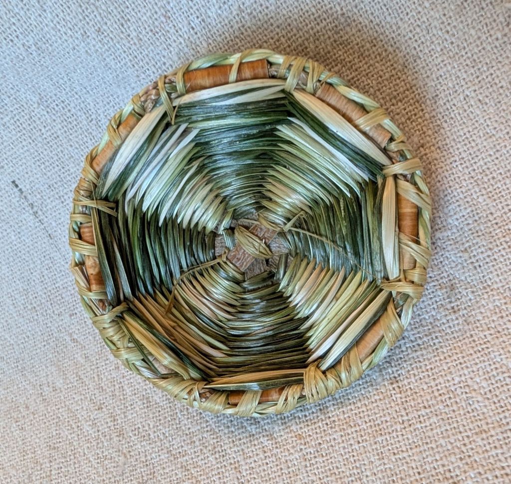 Interior view of the finished lid, showing the whip stitching attaching a sweetgrass braid to the outer rim with black raspberry bast fiber ribbon.